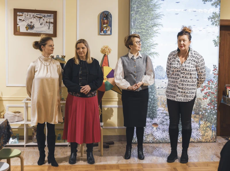 Cztery kobiety stoją obok siebie w sali, a za nimi widoczne są dekoracje i obrazy.