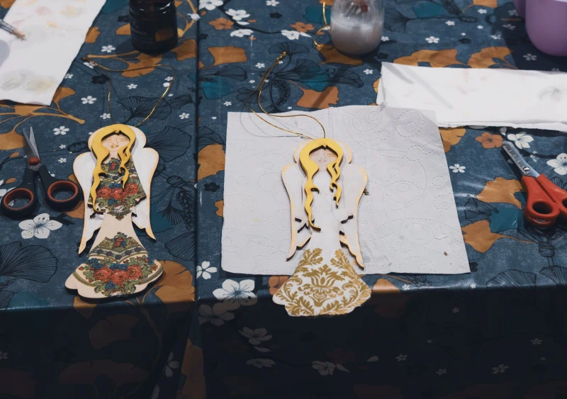 Ręcznie robione papierowe aniołki leżące na stole z materiałami do prac plastycznych.