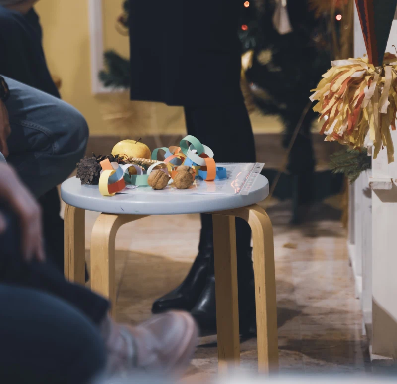 Mały stolik z papierowymi łańcuchami i orzechami, otoczony przez siedzące osoby.