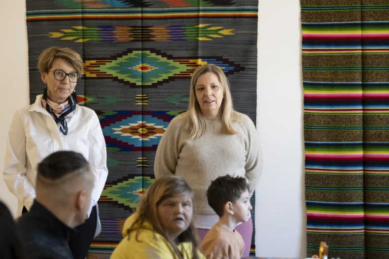 Dwie kobiety stoją przed grupą uczestników warsztatów na tle kolorowych tkanin.