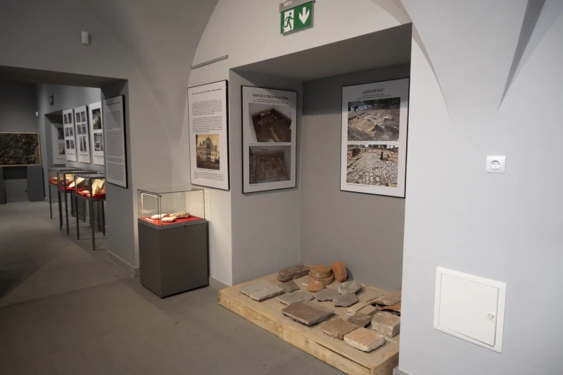 „Wnętrze wystawy historycznej z eksponatami w szklanych gablotach i materiałami informacyjnymi dotyczącymi odkryć archeologicznych.”