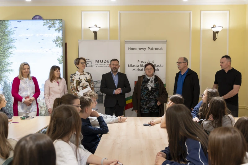 Laureaci konkursu Mój Region 2026 siedzą przy stołach, słuchając przemówienia organizatorów w sali muzealnej.