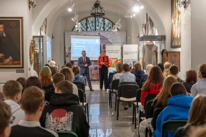 Uczestnic siedzący na krzesłach i słuchajacy przemowy.