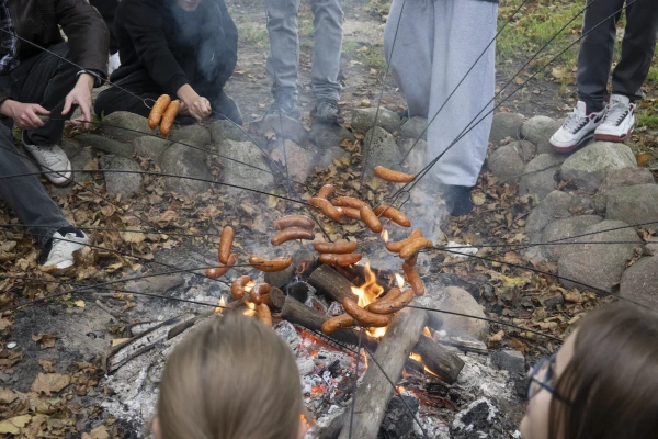 Uczestnicy pieką kiełbaski nad ogniskiem.